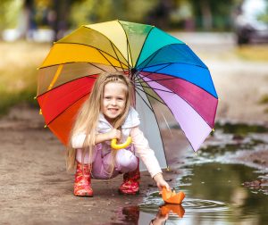 Girl-with-colorful-umbrella-making-paper-ship-sail-in-puddle-happy-childhood